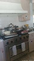 Multiple pots and pans, baking sheets, and cookware arranged on a stovetop and countertop