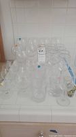 Multiple clear stemmed wine glasses and brandy glasses on a tiled countertop