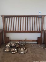 Front view of the wooden headboard leaning against a wall with silverware and trays on the floor in front of it.