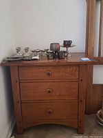 Wooden nightstand with three drawers shown from a front view with various glassware items on top.
