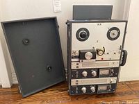 Front view with hinged cover removed showing full unit with tape reels, transport controls, dual channel modules and carry handle
