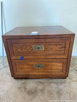Front view of vintage wood nightstand showing two drawers with brass keyhole hardware on a wood grain finish.