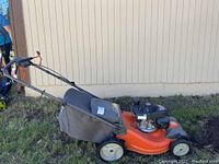 Side view of orange deck, black fabric grass bag, tubular handle and wheels