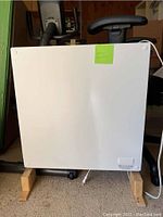 Front view of the white ceramic flat panel heater on wooden block supports with attached power cord visible.