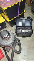Photo showing the red and black Shop Vac wet/dry vacuum with hose and black plastic battery case containing Ever Start battery.