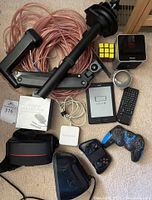 Lot items laid out on carpet background, showing VR headset, monitor mount arm, Kindle, controllers, cables, AC adapter box, wireless keyboard, Haspeeder device, and a Rubik's cube