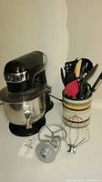 Photo showing the kit of Cuisinart stand mixer with stainless steel bowl and container with utensils including spatulas, tongs, and spoons.