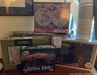 A group of five assorted puzzles stacked: a Eurographics 2000-piece vintage world map on top, an Olympic National Park 1000-piece on the left, Beautiful Yosemite 550-piece by Elk & Elk in front, a wooden puzzle to the right, and another 1000-piece puzzle with architectural theme visible.