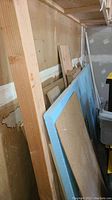 Various wood boards, pegboard, and blue foam insulation board leaning against wall