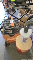 Overview photo showing orange and black Ridgid wet/dry vacuum with attached Dust Deputy cyclone separator on a wooden base and hoses.