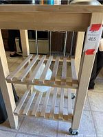 Front lower part of wooden kitchen cart showing slatted shelves and caster wheels.