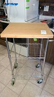 Full view of the rolling cart showing the bamboo cutting board top, metal frame with wire shelves, and caster wheels.