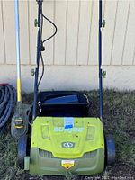 Front view of Sun Joe electric dethatcher unit showing green body, wheels, handle, and grass collection bag attached at rear. Visible wear and dirt on body.