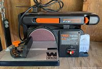 Front and side view of WEN belt and disc sander showing sanding belt, disc, miter gauge, on/off switch, and WEN branding.