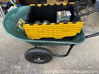 Green Yard Rover wheelbarrow with black metal frame and pneumatic tires containing a yellow and black tool organizer box and miscellaneous items inside.