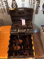Open black plastic case with wrench set and socket bits above yellow bin containing various clamps.