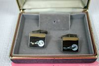 Front angle view of the pair of sterling silver cufflinks in a display case, showing the bird and moon design with mother of pearl and abalone inlays.