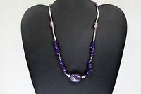 Full view of necklace displayed on black bust, showing silver tone bars and amethyst beads, including a large central oval bead.