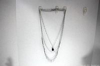 Front view of the three strand silver color necklace with blue stone pendant on a black holder against a white background.