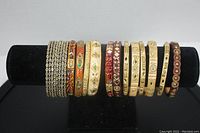 Front view of 13 assorted bangles arranged on black bracelet stand showing overall variety of colors and textures.
