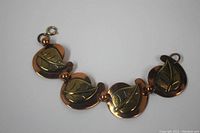 Full view of brass and copper bracelet with leaf design and hook clasp, showing four leaf motifs and connecting beads.