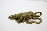 Side angle view of brass crocodile paper clip showing textured scale design and curled tail, highlighting spring mechanism.