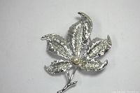 Top view of vintage Coro silver flower brooch showing textured five leaves with a pearl center on white background.