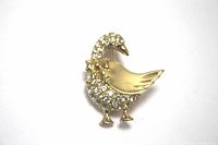 Front view of gold-tone duck brooch with clear rhinestones and gold bow on neck, set against a white background.