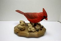 Front and side view of hand painted red cardinal bird on wooden base with carved rocks and black berries.