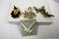 Four decorative brooches placed on white display board: clown with red enamel, rhinestone swan, rhinestone butterflies, and handcrafted white seagull.