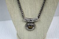 Close-up of the pendant showing the tiger eye stone and decorative oval setting on the silver tone thick chain.