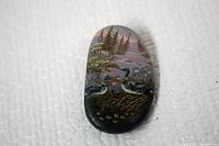 Clear image of the front of the stone brooch showing the detailed oil painting of two geese by water and trees.