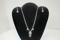 Full view of the rhinestone necklace and matching earrings displayed on a black bust form.