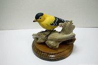 Side view of gold finch bird sculpture perched on branch with wooden base