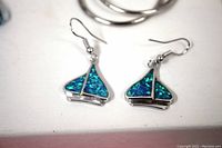 Close-up photo of blue-green opal-like sailboat earrings with hook backs, showing detail and size