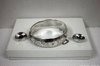 Front view of the sterling silver bracelet with floral engraving and matching earrings on display stand.