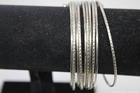 Silver tone cuff bracelet displayed on black jewelry holder showing ten parallel thin rows with alternating plain and patterned designs.