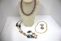 Photo showing two necklaces on a display bust and one gold tone brooch with rhinestones and faux pearl on a white surface.