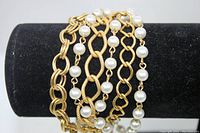 Gold tone six-strand chain bracelet with faux pearls displayed on black velvet background.