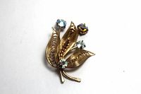 Copper flower brooch with intricate leaf design and AB rhinestones on white background, showing front details
