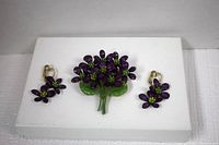 Photo of the vintage purple enameled flower brooch and matching clip-on earrings on a white background.