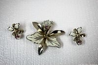 Orchid flower brooch and matching screw-on earrings laid flat, showing front design with enamel petals and pink rhinestone centers.