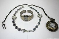 Photo showing three wrist watches and one pocket watch with chain laid on white background for condition and detail inspection.