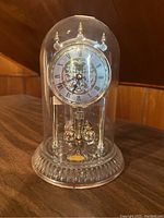 Bulova lead crystal clock under dome with visible clock face and rotating pendulum.
