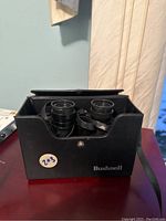 Front view of black Bushnell binoculars inside black carrying case with a snap-button closure and strap.