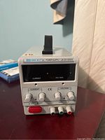 Front view of LW-3010KDS DC Power Supply showing analog current and voltage meters, adjustment knobs, and output terminals.