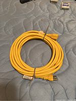 Yellow heavy duty extension cord coiled on a quilted surface, with visible male plug and female socket ends, bound with cable ties.