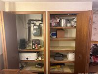 Two shelving units showing various kitchen appliances including a slow cooker, coffee grinder, spice bottles, metal pot, rice cooker, and other household items.