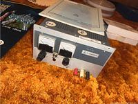 Photo of Lambda regulated power supply unit with analog meters, knobs, and output terminals on front panel, resting on an orange carpet.