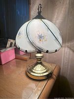 Photo of vintage brass table lamp with blue and gold floral hand-painted glass shade, lamp shown on wooden table
